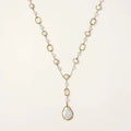 Y-shaped gold necklace with alternating geometric links, freshwater pearls, and baroque pearl pendant on cream background