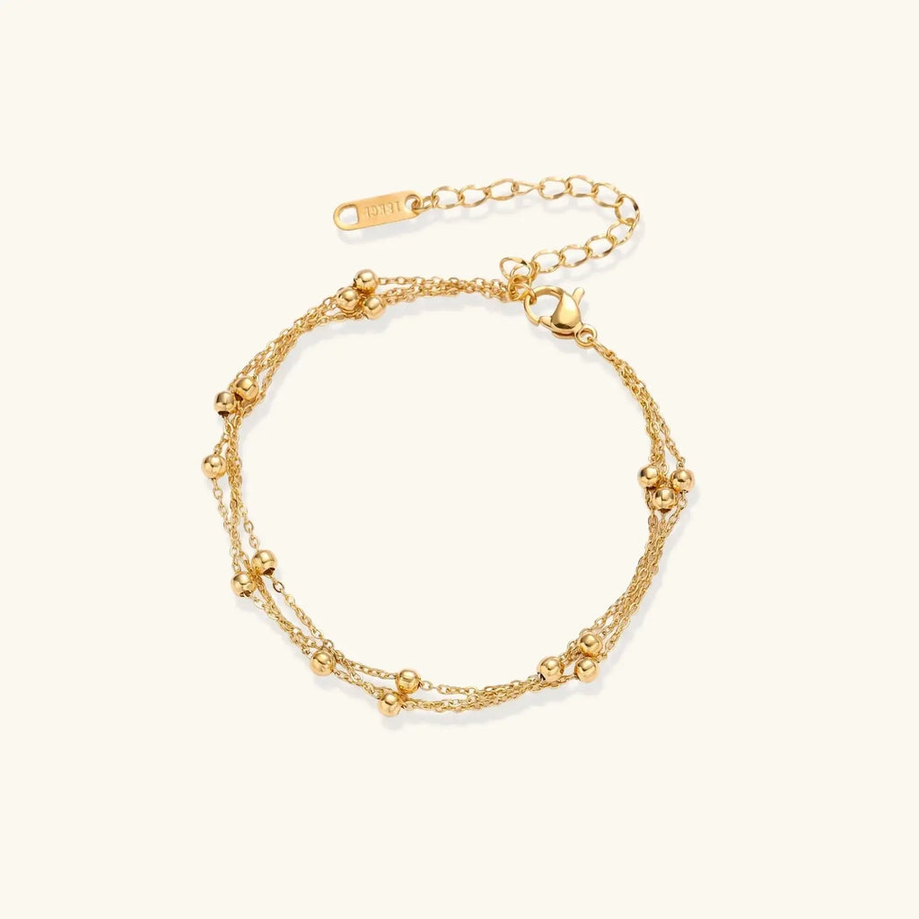 Three-strand gold-plated bracelet with clustered ball beads and adjustable clasp on cream background