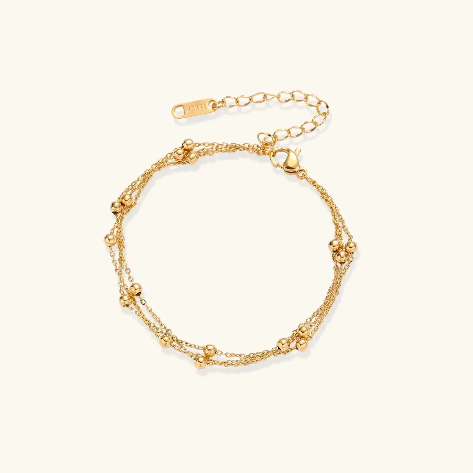 Three-strand gold-plated bracelet with clustered ball beads and adjustable clasp on cream background