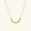 Delicate gold-plated necklace with graduated spherical beads forming gentle smile curve on beige background