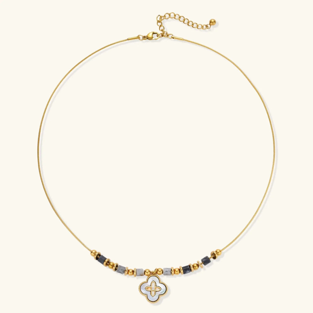 Gold-toned beaded necklace with grey stones and quatrefoil abalone shell pendant on cream background.