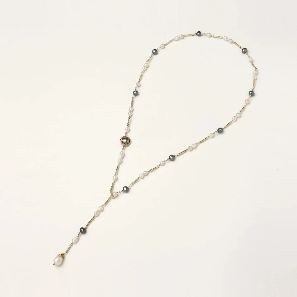 Y-shaped gold-plated necklace with white and gray freshwater pearls on cream background, showing adjustable drop design.