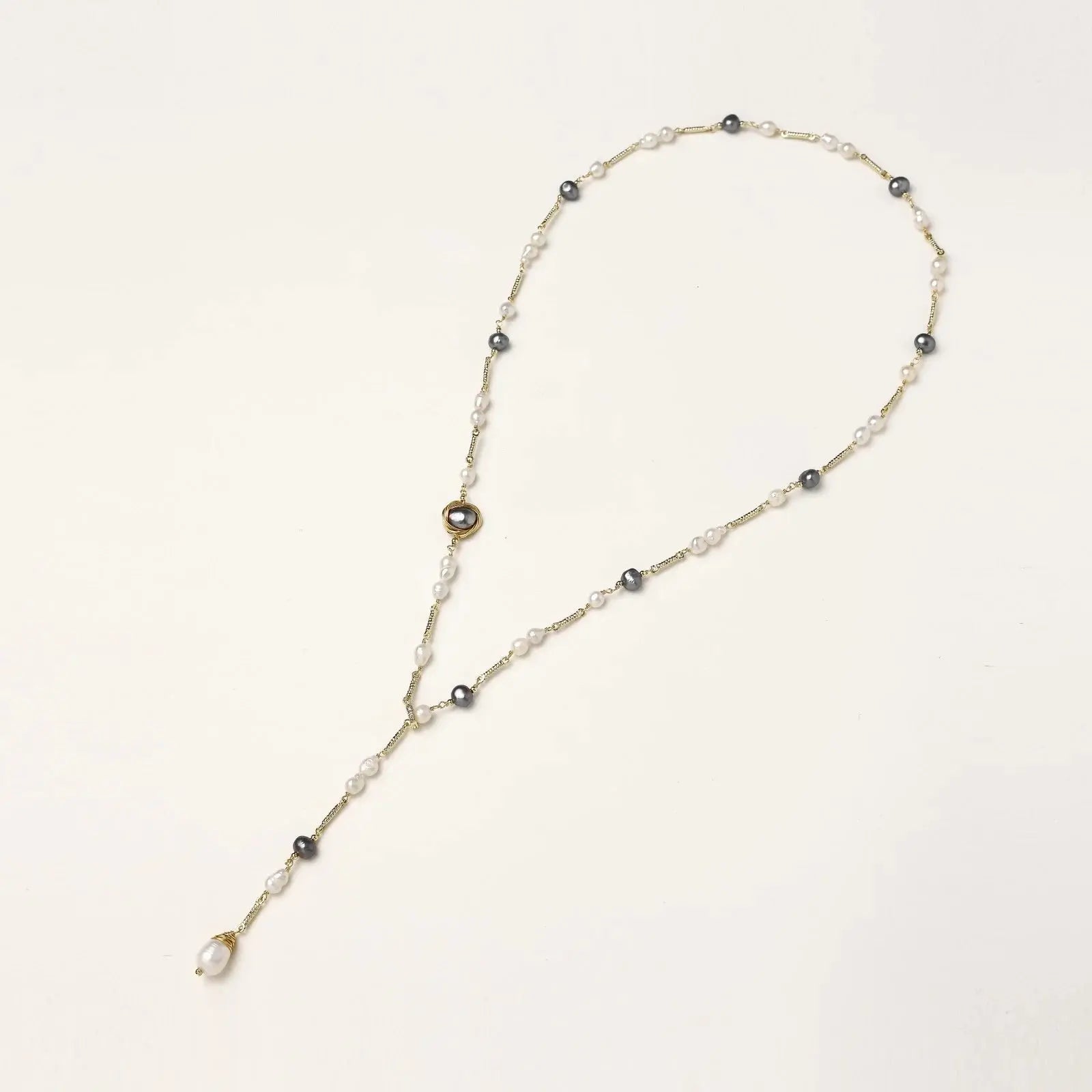 Y-shaped gold-plated necklace with white and gray freshwater pearls on cream background, showing adjustable drop design.